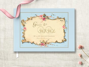 light blue traditional hardcover wedding guest book featuring antique french ephemera frame on the cover with pink floral accent and gold bronze wording personalized with names and wedding date